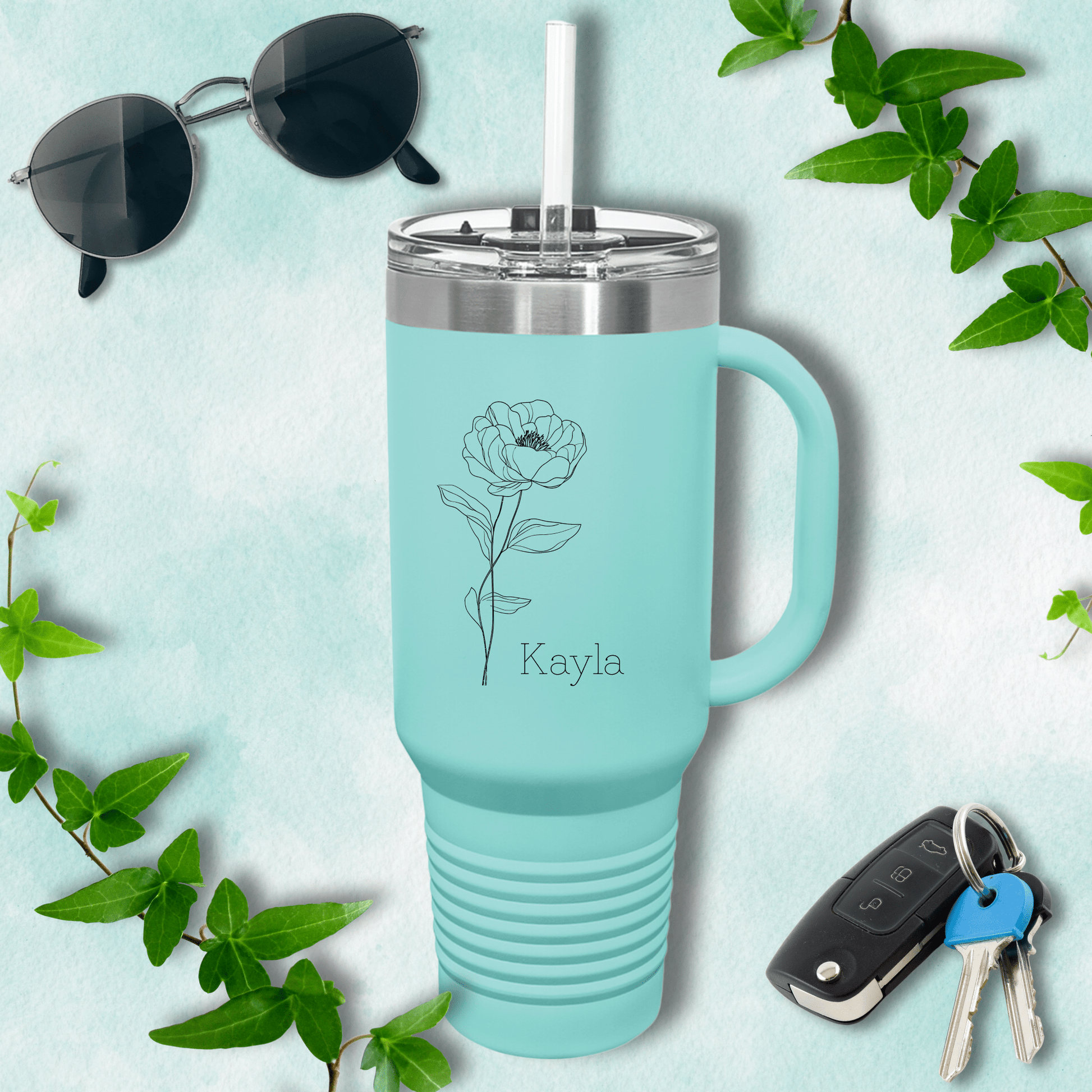 a blue travel mug with a flower on it next to a pair of sunglasses and