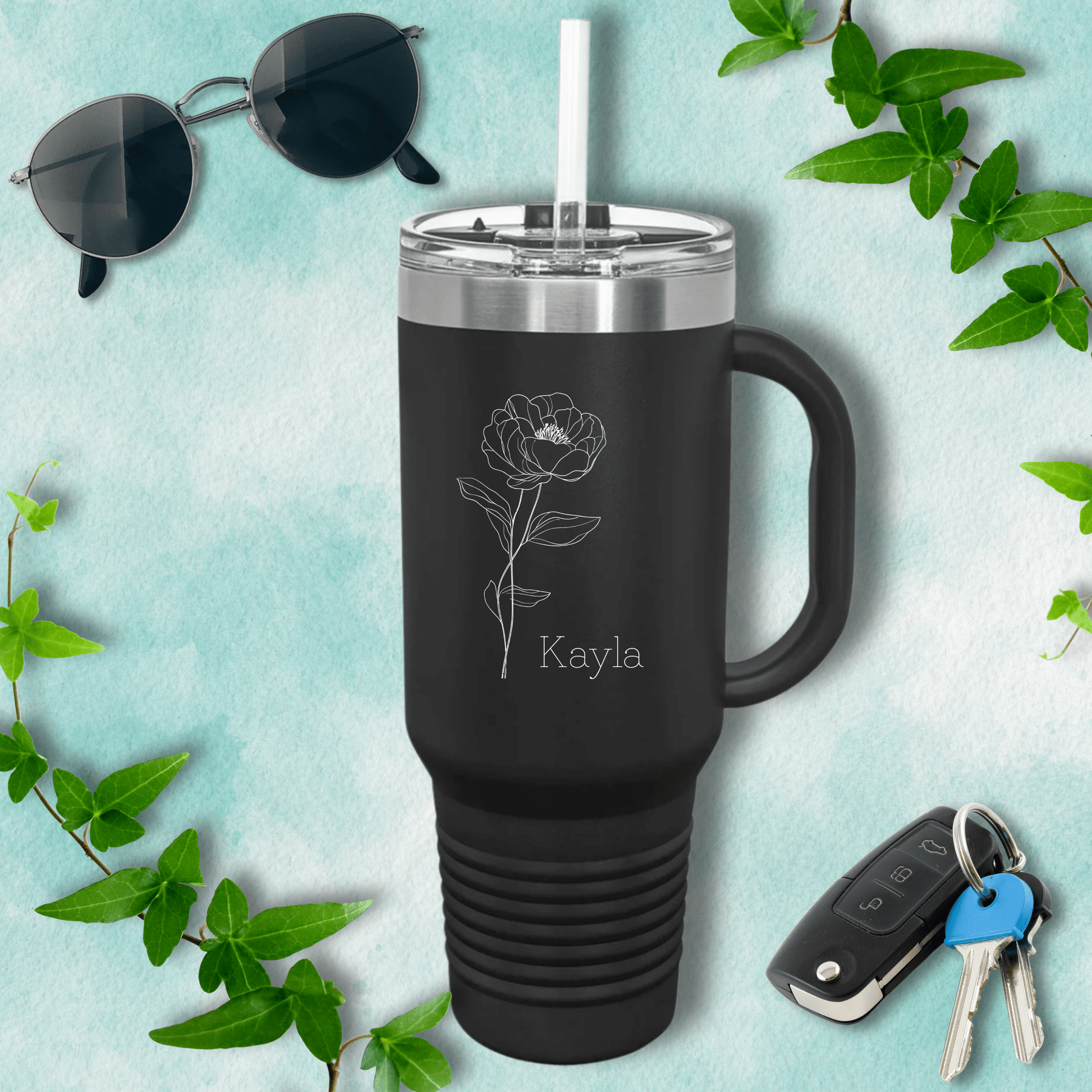 a travel mug with a rose on it next to a pair of sunglasses