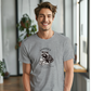 a smiling man wearing a gray shirt with a raccoon on it